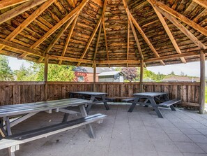 Een overdekt picknickgedeelte met houten banken en tafels, omgeven door een houten hek.