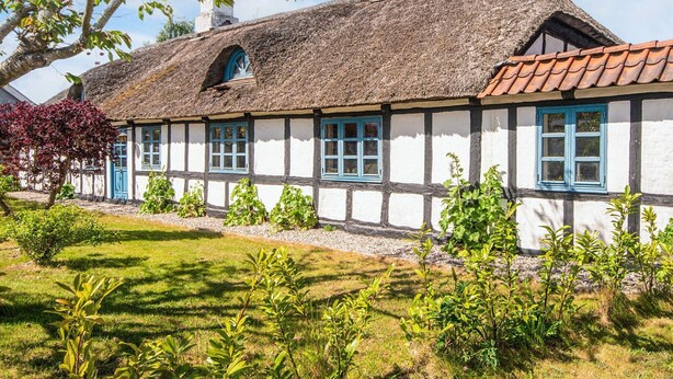 A traditional half-timbered house with a thatched roof, white walls, and blue window frames.