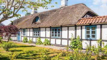 Uma casa tradicional em estilo de enxaimel, com telhado de colmo, paredes brancas e molduras de janela azuis.