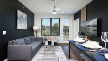 A modern living room with a gray sofa, a coffee table, and a dining area with a table set for two.