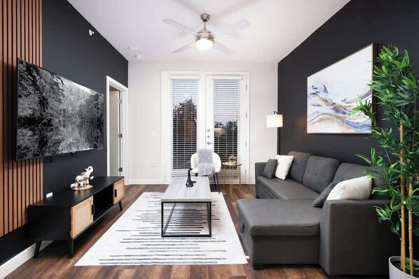 A modern living room with a grey sofa, a coffee table, and a TV mounted on the wall. - Spacious Modern 1-Bedroom, Near Riverwalk & Dome (San Antonio)
