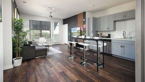 Een moderne keuken met grijze kastjes, een centraal eiland met krukken, en een zithoek met een bank en een salontafel.