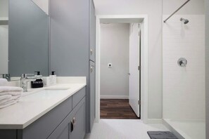 A modern bathroom with a large mirror, two sinks, and a shower.