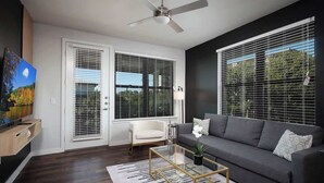 A modern living room with a dark grey sofa, a glass coffee table, a white armchair, and a ceiling fan.