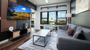 A modern living room with a large flat-screen TV, a sofa, a coffee table, and a dining area with a table and chairs. - Downtown 1-Bedroom Stay with Gym and Free Parking (San Antonio)