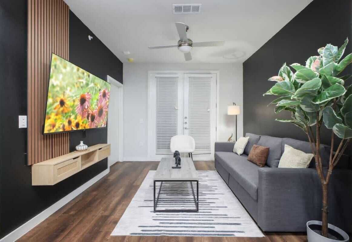 A modern living room with a flat-screen TV, a grey sofa, a coffee table, and a potted plant.