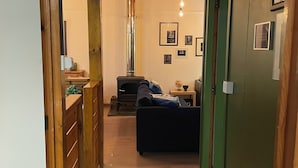 A narrow hallway with wooden walls and a green door, leading to a living area with a sofa and a fireplace. - Relax and take your time at Chalet du temps suspendu (Rendeux)