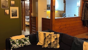 A cozy cabin interior with a wooden ceiling, a sectional sofa with patterned cushions, and a dining table with pinecones. - Relax and take your time at Chalet du temps suspendu (Rendeux)