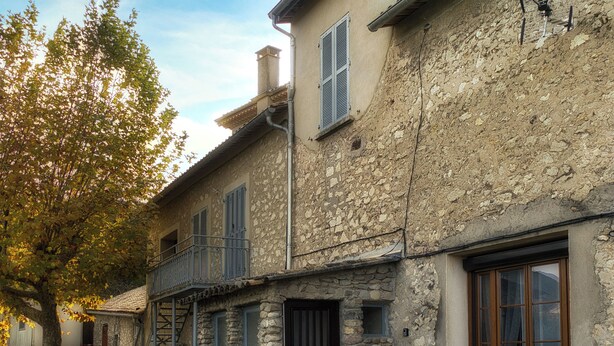 A stone building with a balcony, a black door, and a window with a view of the mountains.
