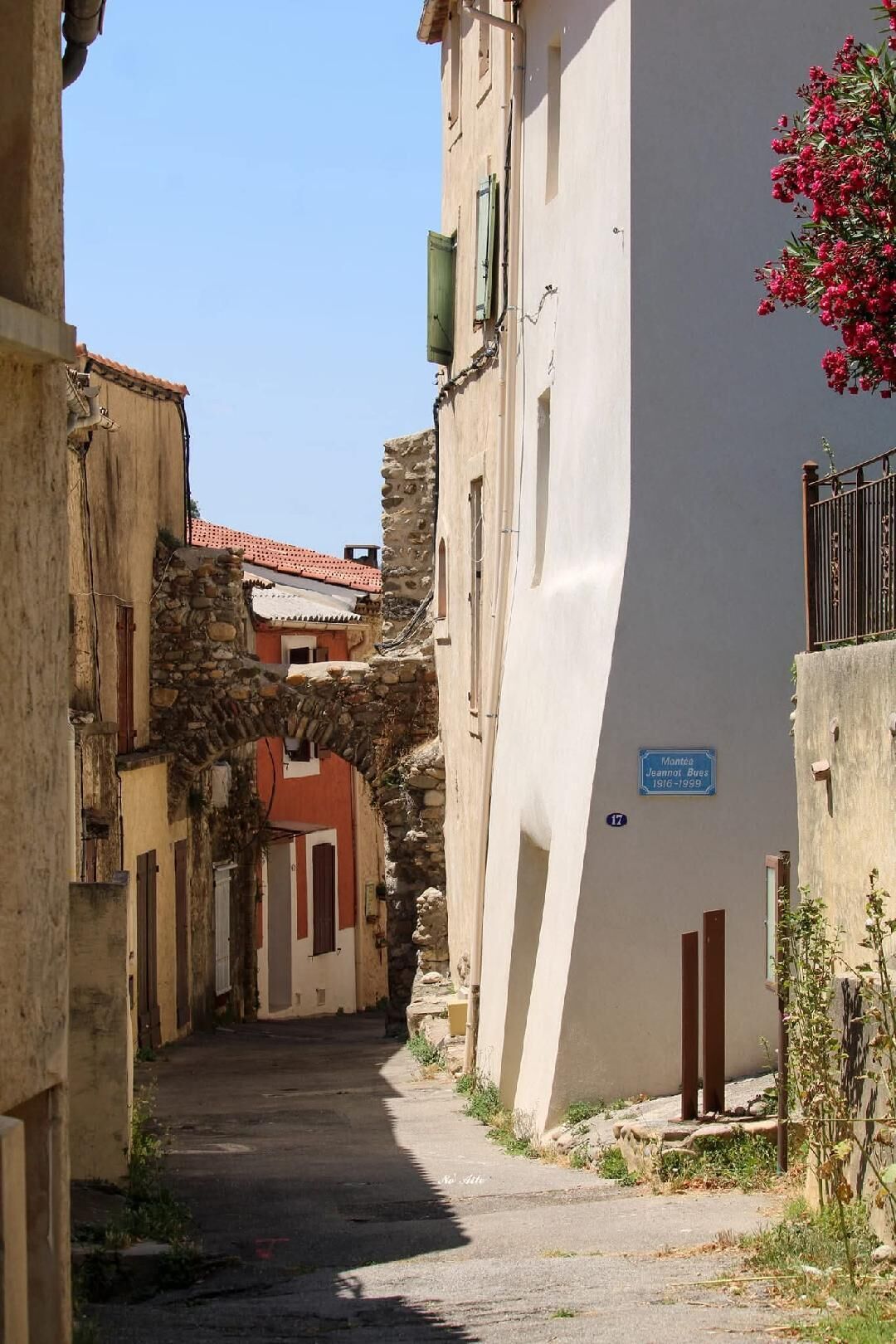 Une rue étroite, bordée de bâtiments des deux côtés, un arc en pierre et une enseigne bleue portant un numéro.
