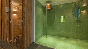 A modern bathroom with a glass shower enclosure, green mosaic tiles, and a wooden door. - Chalet Baker Vacation Home (Pettneu am Arlberg)