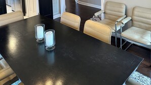 Un comedor con una mesa negra, cuatro sillas y una lámpara de araña. Se ve una escalera que sube a otro nivel.