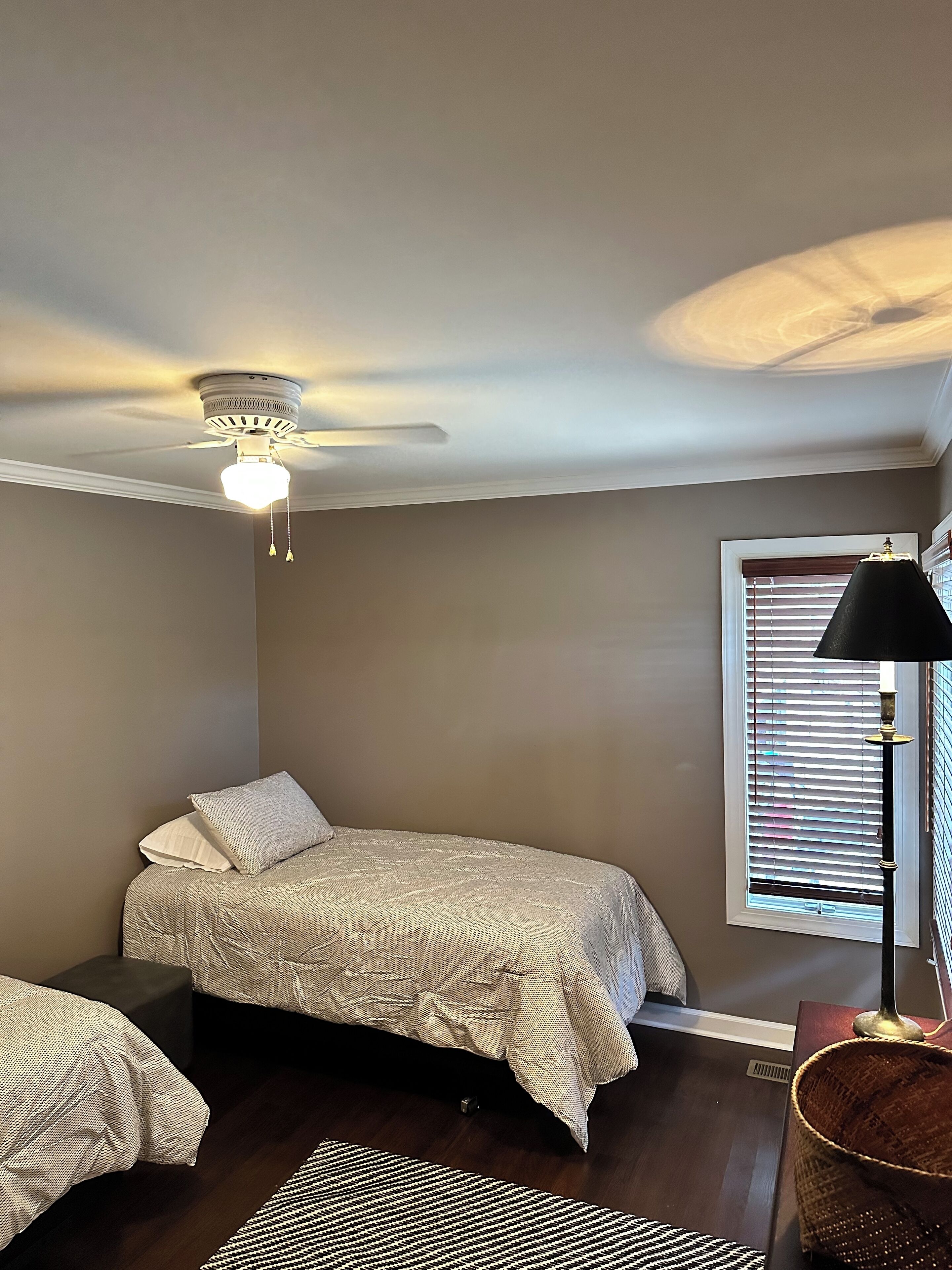 A bedroom with a bed, a ceiling fan, a window with blinds, and a lamp.