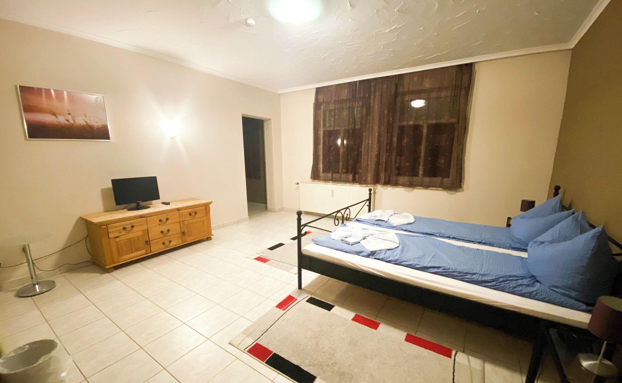 A bedroom with a bed, a wooden dresser, a television, and a window with curtains.