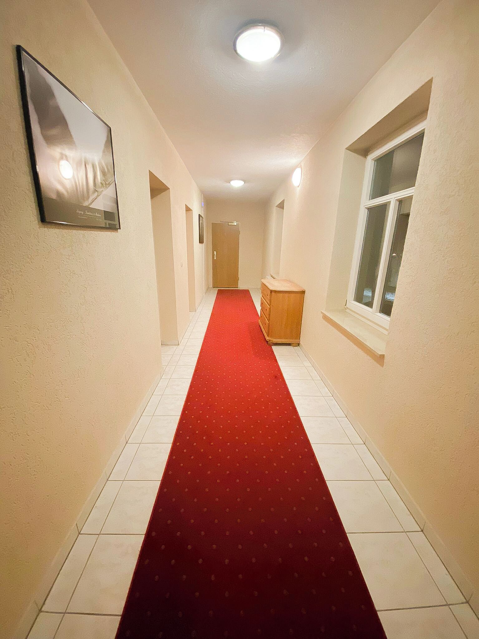 A hallway with a red carpet, white walls, and a wooden cabinet.