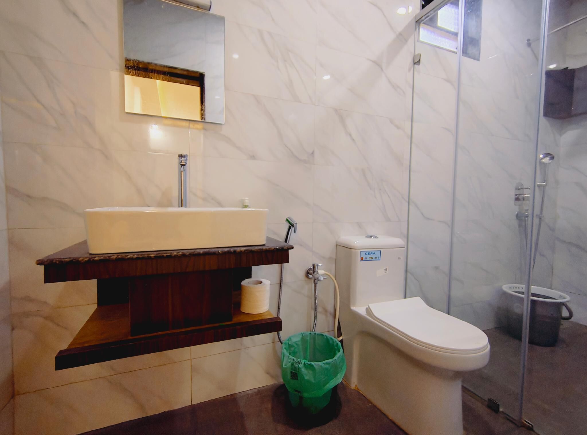A bathroom with a marble wall, a sink, a toilet, and a shower enclosure.