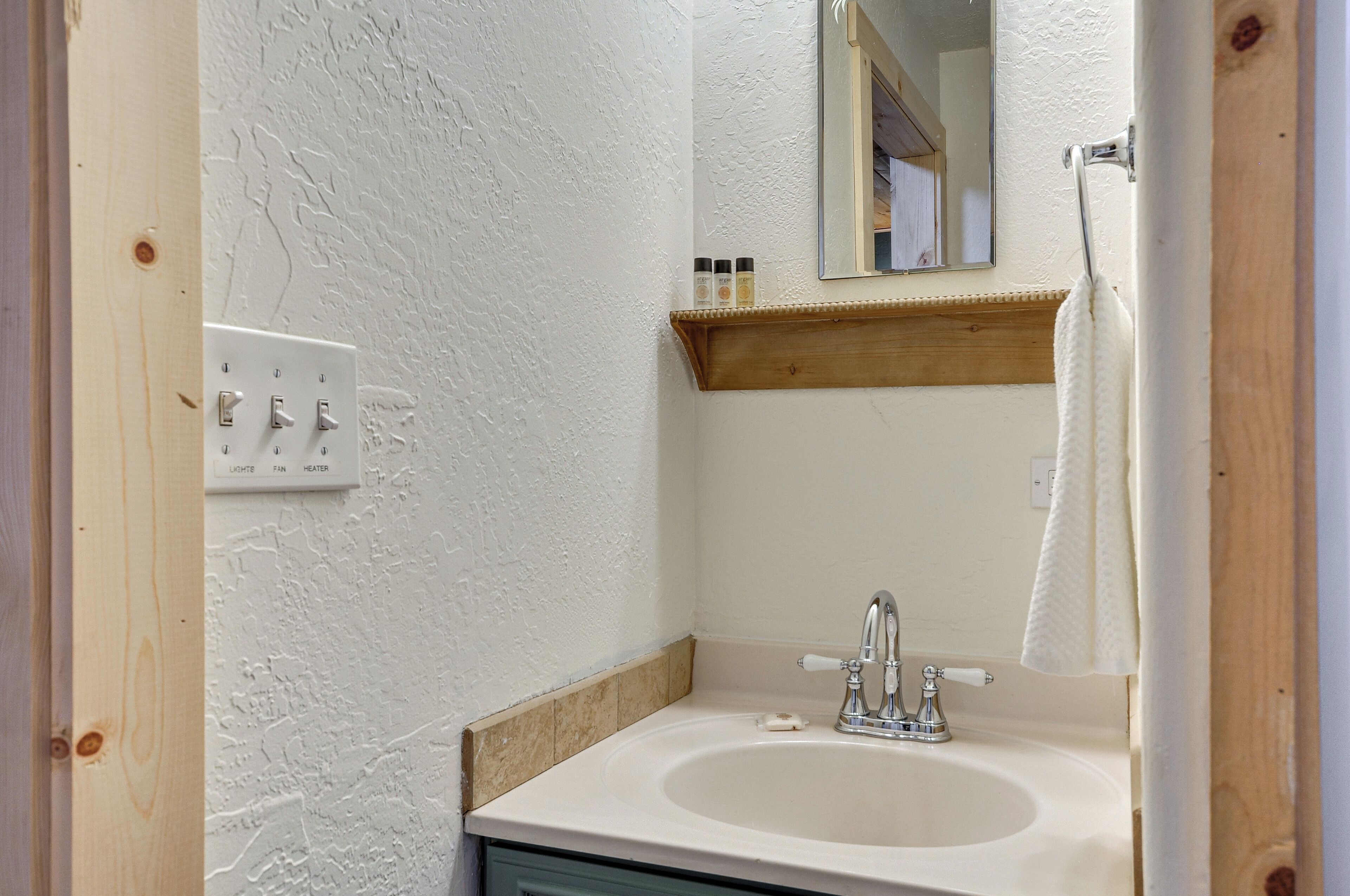 A bathroom with a white sink, a mirror, a towel hanging on a rack, and a shelf with toiletries.