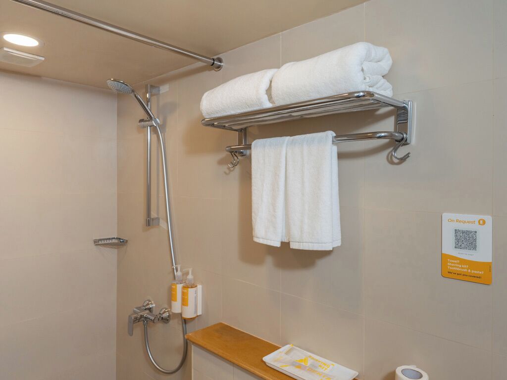 A bathroom with a shower, a towel rack, a soap dispenser, and a sign indicating towel service on request.
