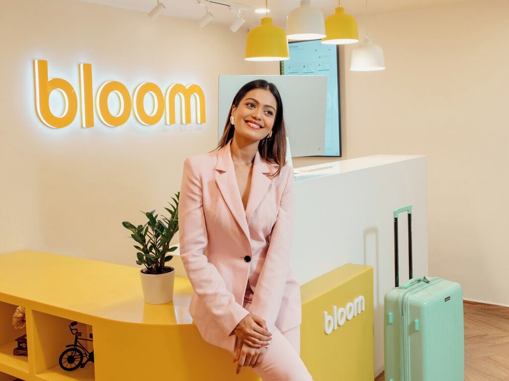 A person sitting on a yellow reception desk with a 'bloom' sign in the background.