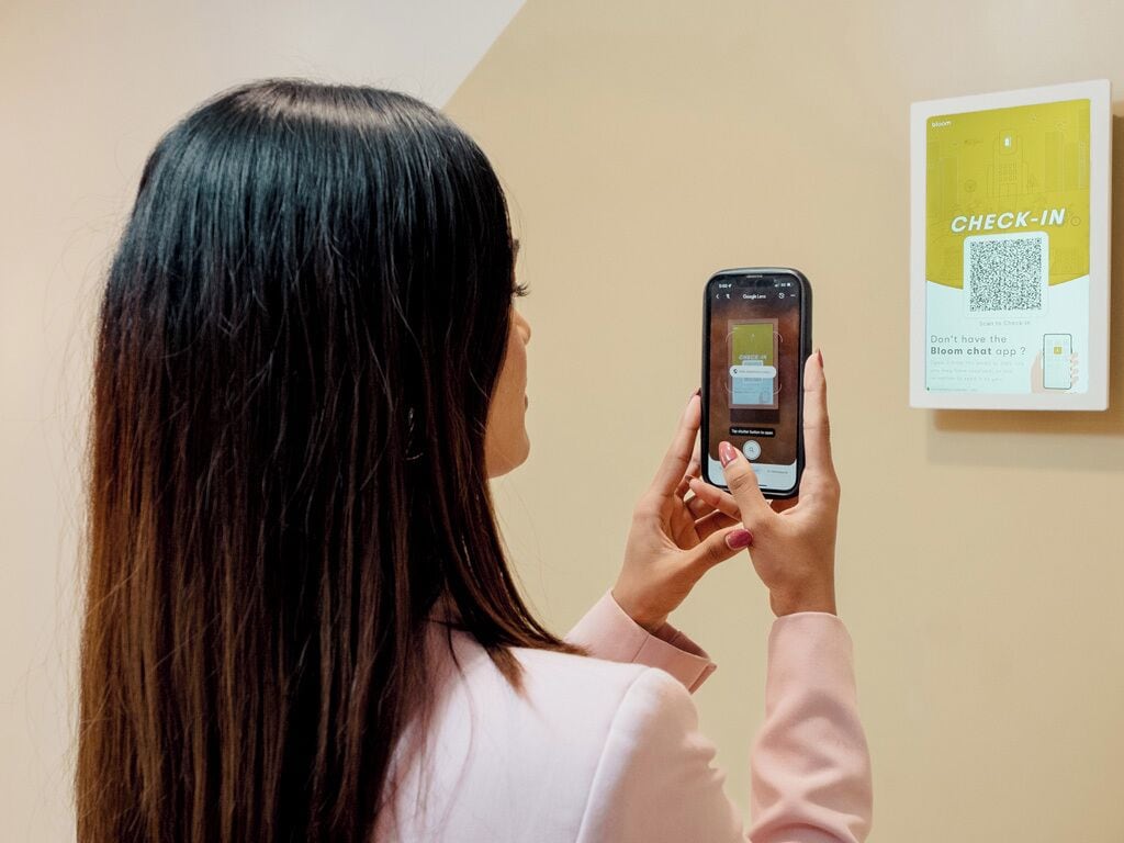 Una persona utilizando un teléfono inteligente para escanear un código QR en un cartel adherido a la pared.