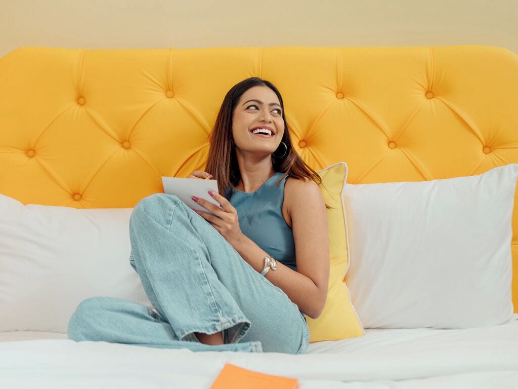 A person sitting on a bed with a yellow headboard, holding a book.
