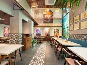 L’intérieur d’un restaurant, avec de nombreuses tables et des banquettes, un sol à motifs et des œuvres d’art murales.