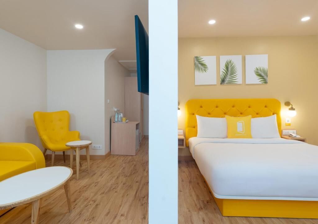 Une chambre d’hôtel avec un lit jaune, un fauteuil jaune, une petite table et un bureau avec une chaise.