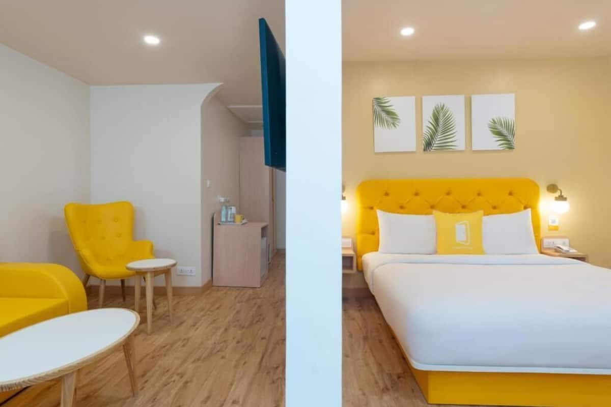 A hotel room with a yellow bed, a yellow armchair, a small table, and a desk with a chair.