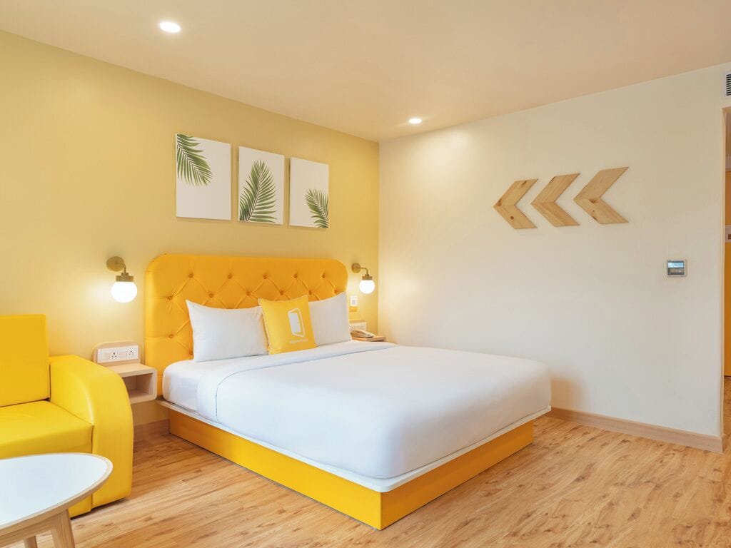 Una habitación de hotel con una cama y un sillón amarillos, además de una mesita.