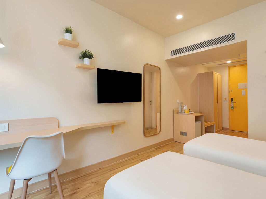 A hotel room with a bed, a desk with a chair, a TV mounted on the wall, and a door leading to a bathroom.
