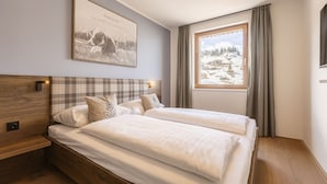 A bedroom with two beds, a wooden headboard, a framed picture on the wall, and a window with a view of a snowy landscape. - Superior Lodge With Balcony (Hermagor-Pressegger See)