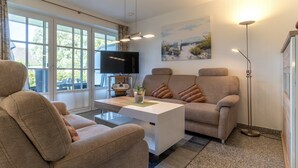 A modern living room with a sofa, a coffee table, a flat-screen TV, and a painting on the wall. - Ferienwohnung fur 4 in St. Peter-ording (St. Peter-Ording)