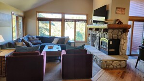 A cozy living room with a stone fireplace, large windows, and a comfortable seating area. - Snowcreek Resort Vacation Rental 733 (Mammoth Lakes)