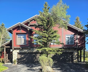 A red two-story house with a stone foundation, a wooden porch, and a large tree in front. - Snowcreek Resort Vacation Rental 733 (Mammoth Lakes)