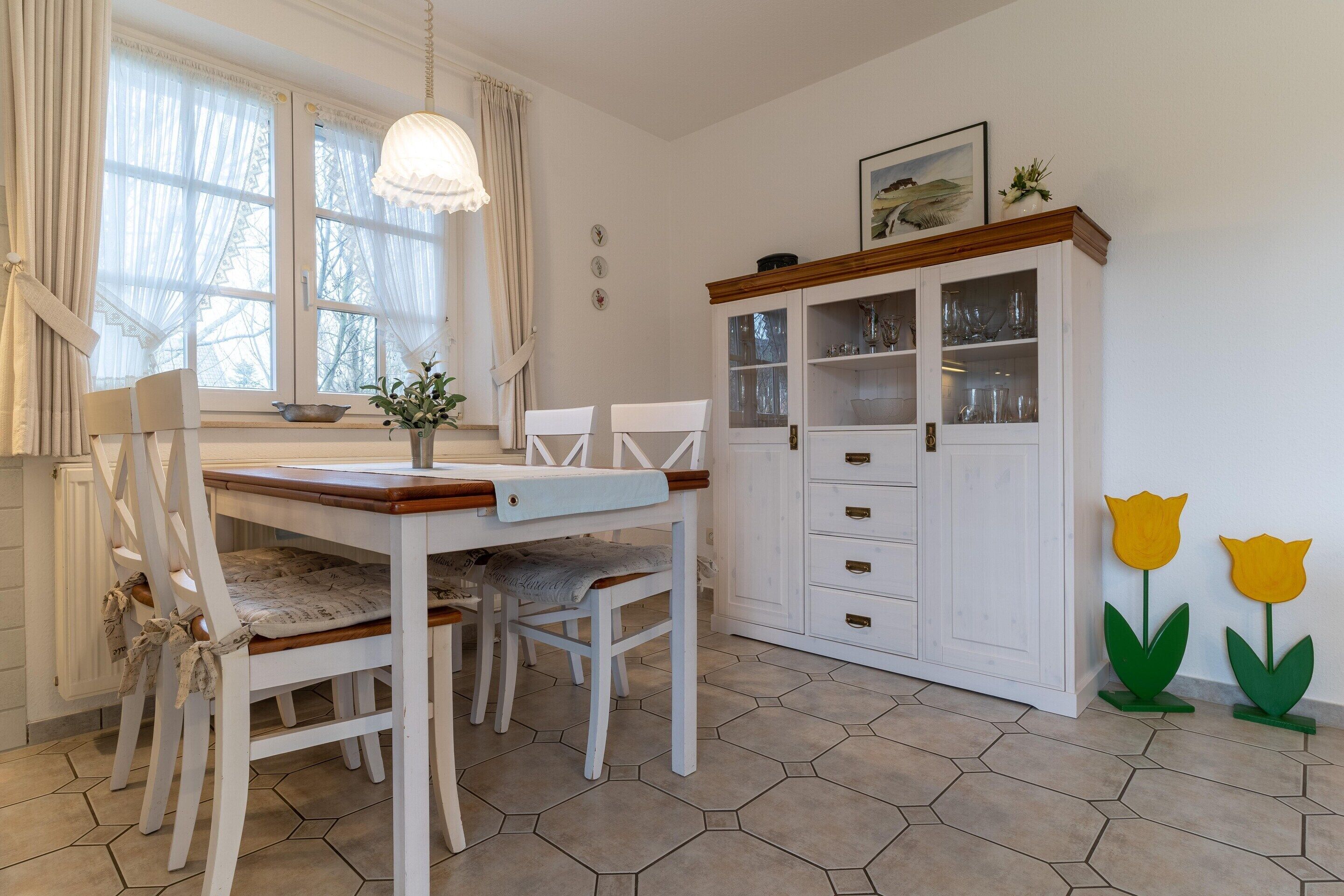 A dining area with a white table, chairs, and a cabinet with glass doors.