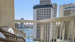 A balcony with wicker chairs and a glass table overlooking a cityscape with high-rise buildings and a body of water. - Central Apt with a Panoramic view over Cairo & Nile (Giza Governorate)