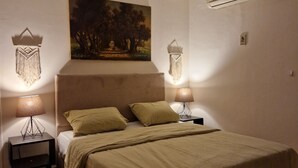 A bedroom with a bed, two bedside tables, a hanging light fixture, a wall-mounted air conditioner, and a painting on the wall. - Central Apt with a Panoramic view over Cairo & Nile (Giza Governorate)