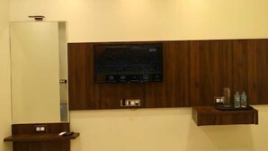A modern bathroom with a large mirror, a mounted television, and a wooden vanity with a tray holding toiletries. - Hotel Harshali Residency (Khalapur)