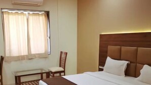 A hotel room with a large bed, a bedside table, a chair, and a window with curtains. - Hotel Harshali Residency (Khalapur)