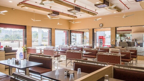 A spacious restaurant with multiple seating areas, large windows, and a visible Coca-Cola refrigerator. - Hotel Harshali Residency (Khalapur)