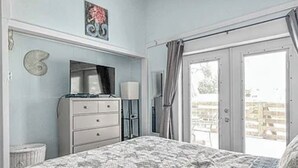 Ein Schlafzimmer mit Bett, Kommode, Fernseher und einem Fenster mit Vorhängen.