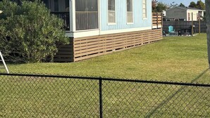 Ein Bungalow mit überdachter Veranda, einem eingezäunten Garten und einer kleinen Terrasse.