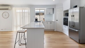 Une cuisine moderne avec des meubles blancs, un réfrigérateur en acier inoxydable et un plancher en bois.