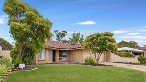 Une maison de plain-pied avec un toit en tuiles, une pelouse bien entretenue et de grands arbres.