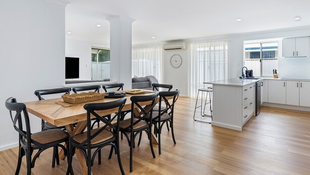 Une cuisine moderne avec des meubles blancs, une table à manger en bois avec des chaises noires et un grand îlot central doté d’un évier.