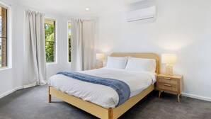 Une chambre avec un lit en bois, deux tables de chevet avec des lampes, une fenêtre avec des rideaux et un appareil de climatisation fixé au mur.