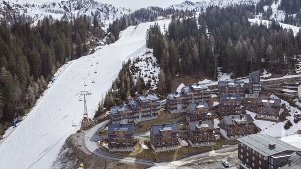 Un centro de esquí con edificios modernos, un telesilla y montañas cubiertas de nieve.