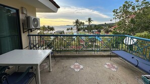 A balcony with a table and chairs, overlooking a pool and palm trees.
