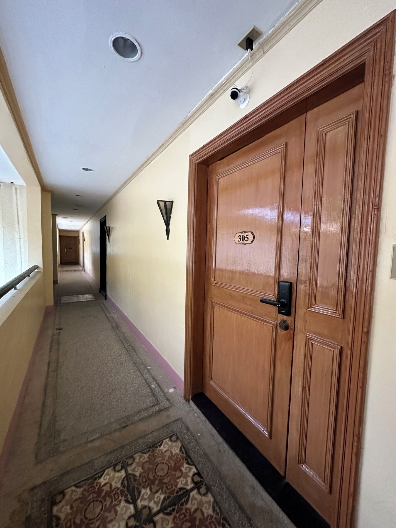 A hallway with a wooden door marked '305', a light fixture, and a patterned rug.
