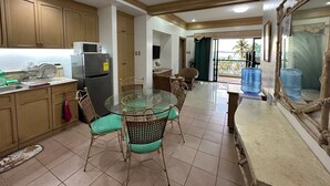 A compact kitchen with wooden cabinets, a refrigerator, and a dining area with a glass table and wicker chairs.
